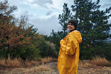 Lonely woman in a vibrant yellow raincoat standing on a rural road in the forest surrounded by trees