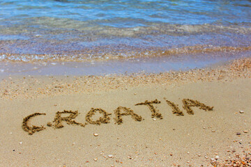 Croatia delicately inscribed in sandy beach as waves approach. Blue sea glistens under summer sun, creating idyllic scene. Tranquil waters and sandy shores inspire beach vacation
