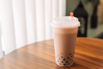 Chocolate bubble tea in a plastic glass with a lid on a wooden table.