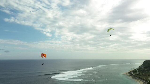 Aerial view of a group of people paragliding near the ocean and cliff in Bali. Extreme leisure for tourists. Flight with a parachute near the sea, a picturesque view of the coast. Summer holidays.