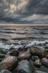 Fototapeta premium An endless sea with rocks on the shore, dark clouds in the sky at sunset. Waves crash against stones in a distant