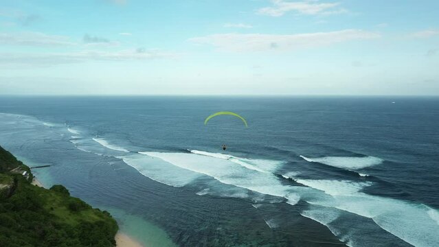 Aerial view of a group of people paragliding near the ocean and cliff in Bali. Extreme leisure for tourists. Flight with a parachute near the sea, a picturesque view of the coast. Summer holidays.