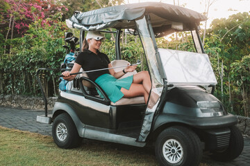 Young attractive professional female golfer sitting in a golf cart next to the green wearing...