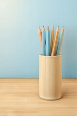Obraz premium Wooden pencil holder filled with colored pencils stands on a wooden desk against a soft blue background, evoking a calm study atmosphere symbolizing knowledge and education, learning, study