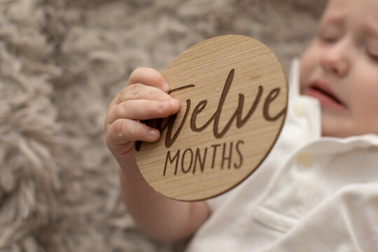 BABY HOLDING A TWELEVE MILESTONE WOOD CIRCLE SIGN 