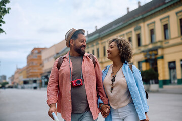Naklejka premium Happy traveler couple talking while holding hands and walking on street.