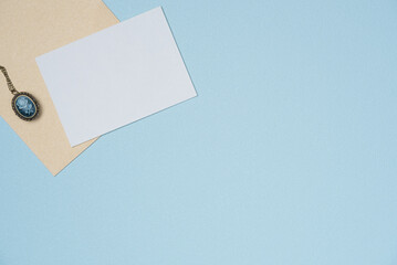 Envelope and empty white paper list with medallion in vintage style on blue background from above. Copy space