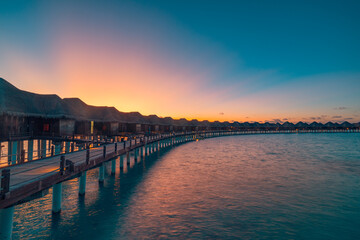 Fototapeta premium Amazing travel beach luxury landscape. Beautiful Maldives tourism sunset seascape view. Horizon colorful sea sky, over water villa pier pathway led lights. Tranquil island, vacation travel background