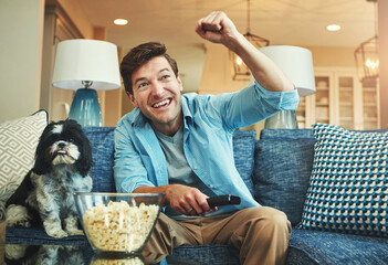 Celebrate, dog and man with popcorn on sofa watching sports match on television at home. Happy,...