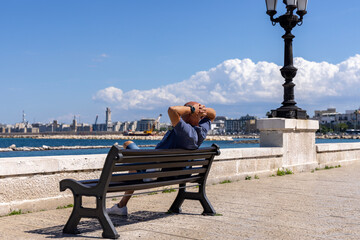 Man resting on a bench at Emperor Augustus seafront (Lungomare Imperatore Augusto), promenade by...