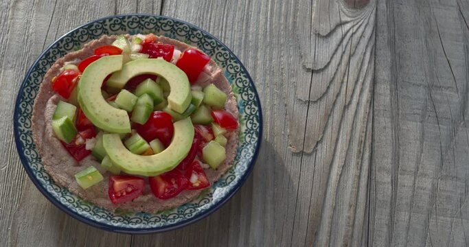 Red corn tortilla topped with Pico de Gallo salsa and avocado slices on a small plate. Rustic wooden background with copy space. Table spin.