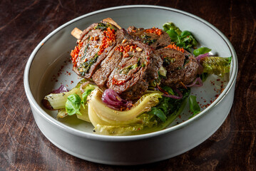 Herb-crusted beef chops on mixed greens, garnished with red spices.