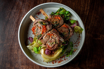 Herb-crusted beef chops on mixed greens, garnished with red spices.