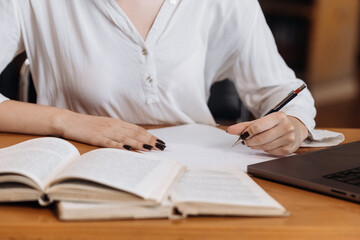 Unrecognizable girl student holding book, making notes at the table, desk in modern university campus library. Education concept, knowledge, wisdom, graduate.