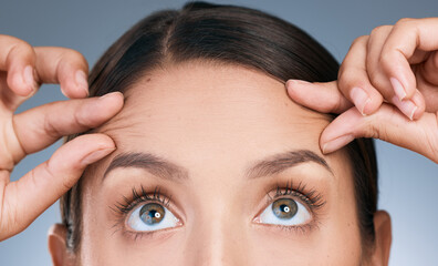 Close up, woman and hands on forehead in studio for skin care, wellness and thinking of facial. Eyes, filler and idea for dermatology by blue background with cosmetics and collagen for detox