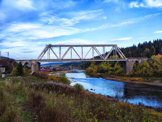 Steel Bridge Over River in Vibrant Autumn Forest on Clear Day