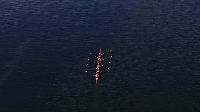 Aerial view of rowing team synchronizing strokes on calm waters at twilight, creating ripples on the lake. Sports and outdoor concept
