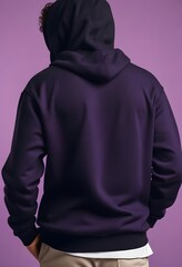 A young man wearing a black hoodie, standing against a purple background