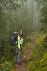 a woman with a big backpack on a hike in the mountains, on the background of a foggy forest, tourism, trekking, a route, a path in the forest, active recreation, nature, adventure, the Carpathians