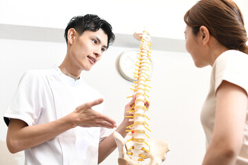 骨の模型を使い女性患者に説明する男性医師