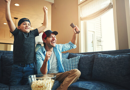 Television, kid and man with success on sofa for network, streaming and watching sports together. Son, dad and popcorn with tv remote in fist for celebration, bonding and live broadcast of match
