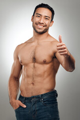 Fototapeta premium Thumbs up, fitness and Asian man in portrait with smile, body positivity and topless in studio. Happy person, approval and proud of progress from exercise, wellness and goal on gray background