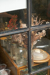 Vases, plants and cups through the frame of a glass window, showing what is inside