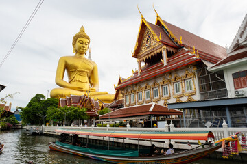 The Giant Budah in the skirts of the river and the canoes passing by xthe water next to a house on the shore