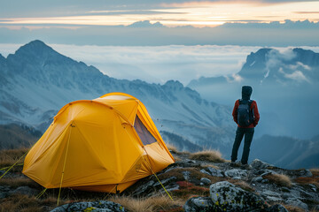 Fototapeta premium Hiker standing near camping tent enjoying inspiring mountains view at sunset
