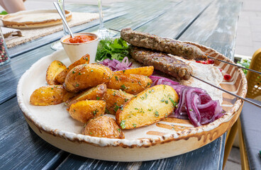 Georgian lula kebab with baked potatoes, sauce and greens. Grilled souvlaki, minced meat kebap,...