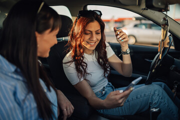 Smiling girls sitting in a car and using cellphone for GPS on journey.