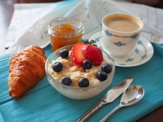 Breakfast in Bed Healthy Oatmeal Porridge, Strawberries, Blueberries, Apricot Orange Jam, Croissant, Cup Coffee on Blue Lagoon Tray Sunny morning Home. Gift Happy Mother's day.Paradise seaside service