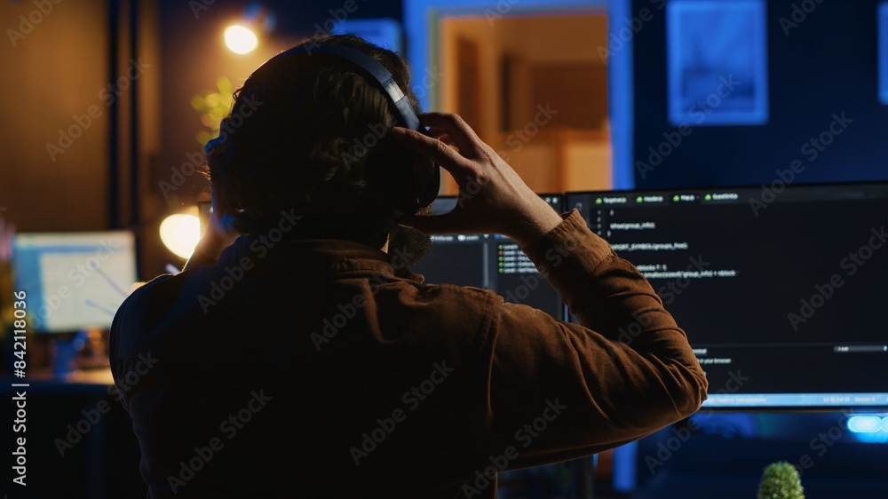 Poster engineer wearing headphones while using coding to fortify security, remotely working for it company.