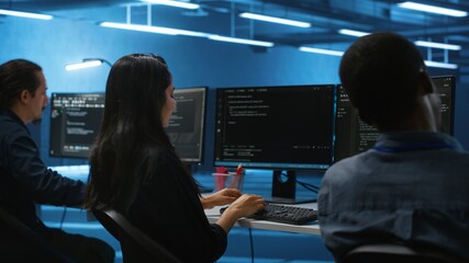 Multiethnic team of engineers working in high tech server hub, using PCs to analyze data....