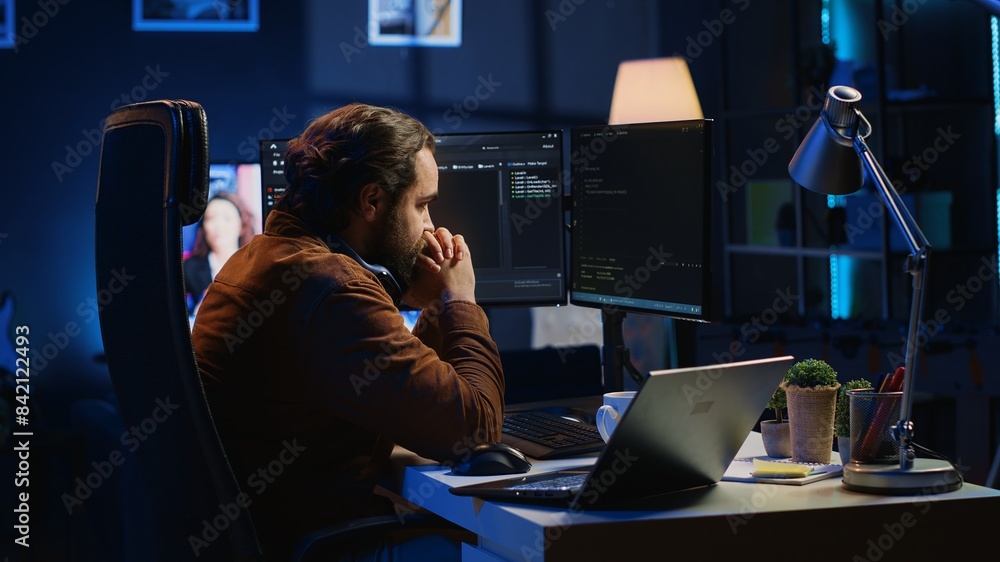Poster technician focused on typing complex code in neon lit home office, developing software application. 