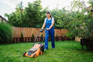 One young caucasian woman is using lawn mower to mow grass in her backyard