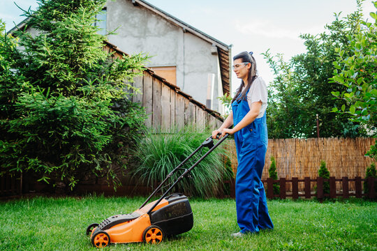 One young caucasian woman is using lawn mower to mow grass in her backyard