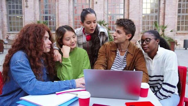 Group of multiracial students doing the high school homework using a laptop computer to search information. Diverse classmates talking and studying together on university campus, learning the lesson