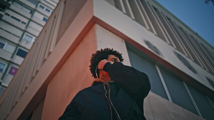 Latino man adjusting earphones at urban building backdrop. Guy listening music