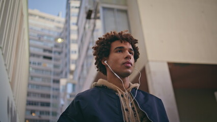 Young melomaniac listening music in headset walking near urban buildings closeup