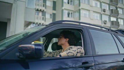 Latino guy sitting automobile looking on city road. Man leaning window car