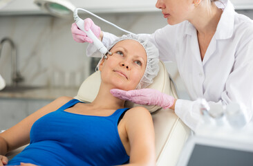 Woman getting facial radio wave lifting skin tightening procedure in beauty salon. RF-lifting...