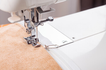 Modern sewing machine special presser foot with beige corduroy fabric and thread, closeup. Sewing...