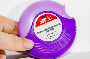 Hand holding purple asthma inhaler on white