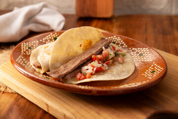 Arrachera Tacos. Marinated beef steak served in a wheat tortilla on a mexican clay plate. Street food from Mexico, traditionally accompanied with cilantro, onion and spicy sauce or guacamole.