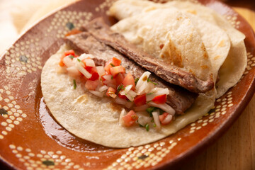 Arrachera Tacos. Marinated beef steak served in a wheat tortilla on a mexican clay plate. Street food from Mexico, traditionally accompanied with cilantro, onion and spicy sauce or guacamole.