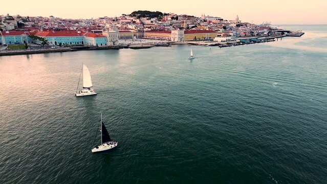 Sailing boats go down the Tagus River past the tourist center of Lisbon, Portugal. Amazing panoramic aerial drone view of an old European city at sunset. High quality 4k stock video