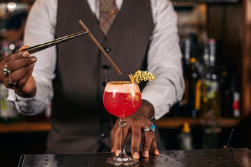 Close-up of an unrecognizable black bartender pouring a cocktail and decorating it with garnish