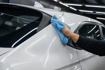 A mechanic wipes the body of a white car with a microfiber cloth. 