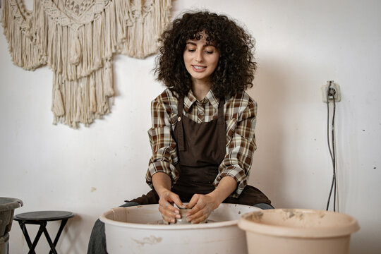 Young female potter working with clay on a pottery wheel in her studio, creating ceramic pieces with focus and creativity.